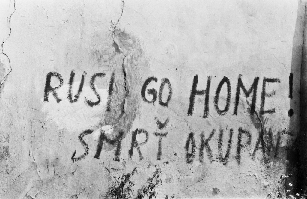 black graffiti on a white wall: RUSI GO HOME! SMRT OKUPANT