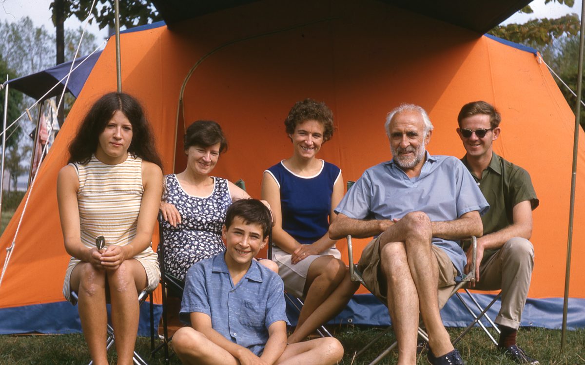 Potrait of six people sitting outside an orange tent smiling at the camera.