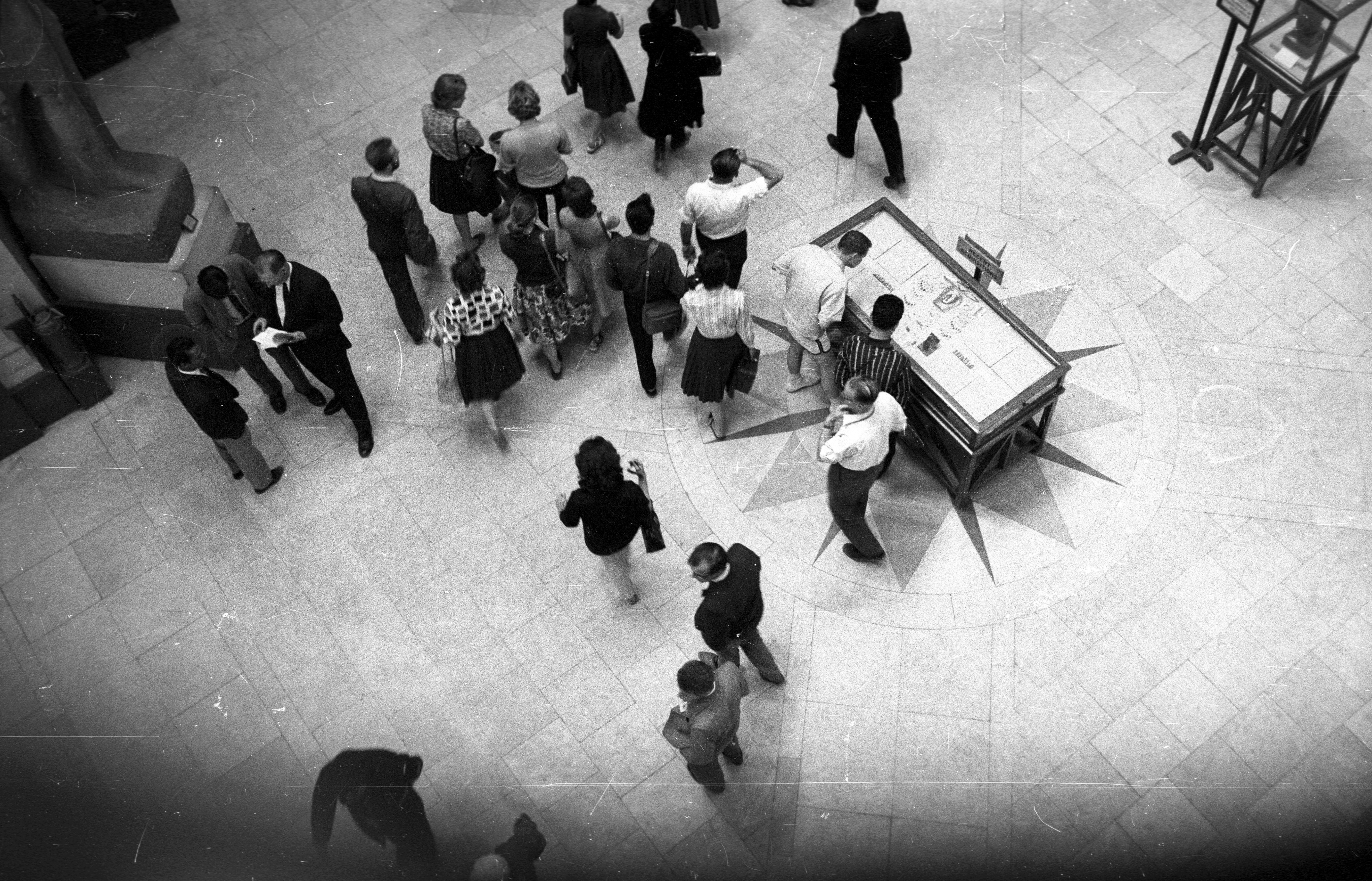 Aerial view of around 15 people walking through an exhibition, two are looking at a display table in the middle of the room